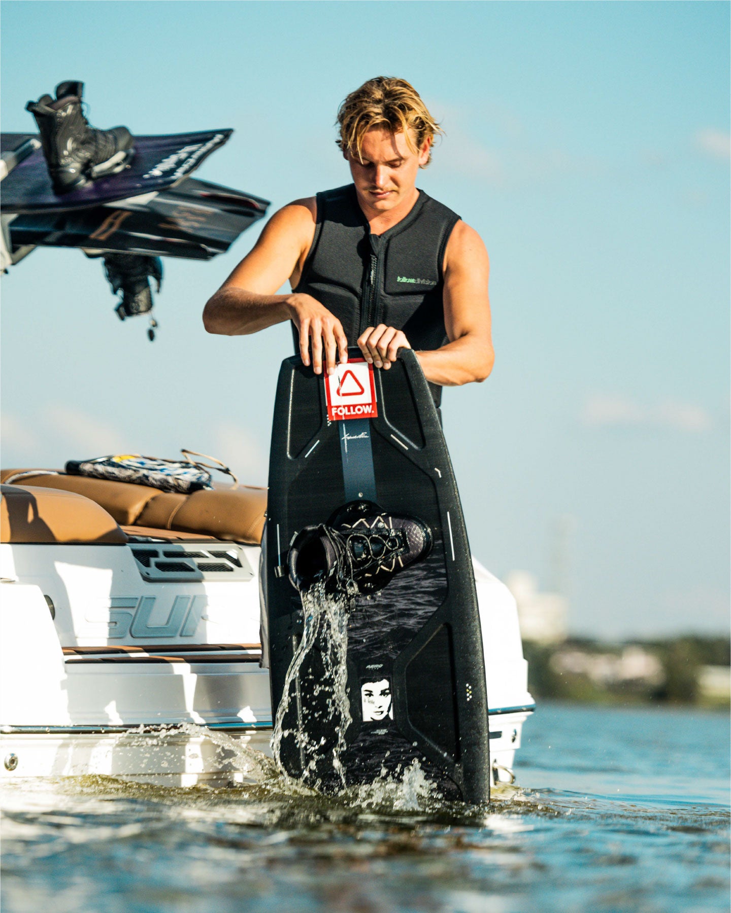 Person preparing to water ski with a wakeboard on a boat in the background
