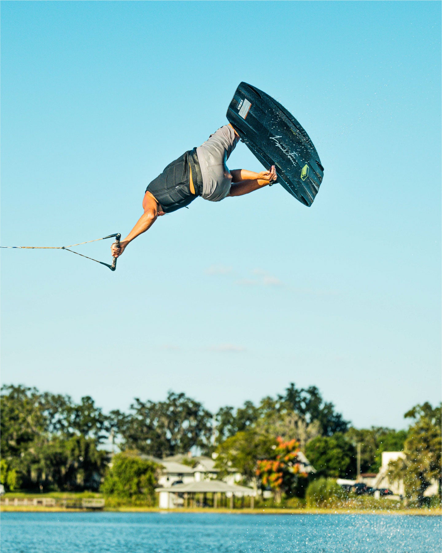 Person wakeboarding in mid-air with a clear blue sky and trees in the background
