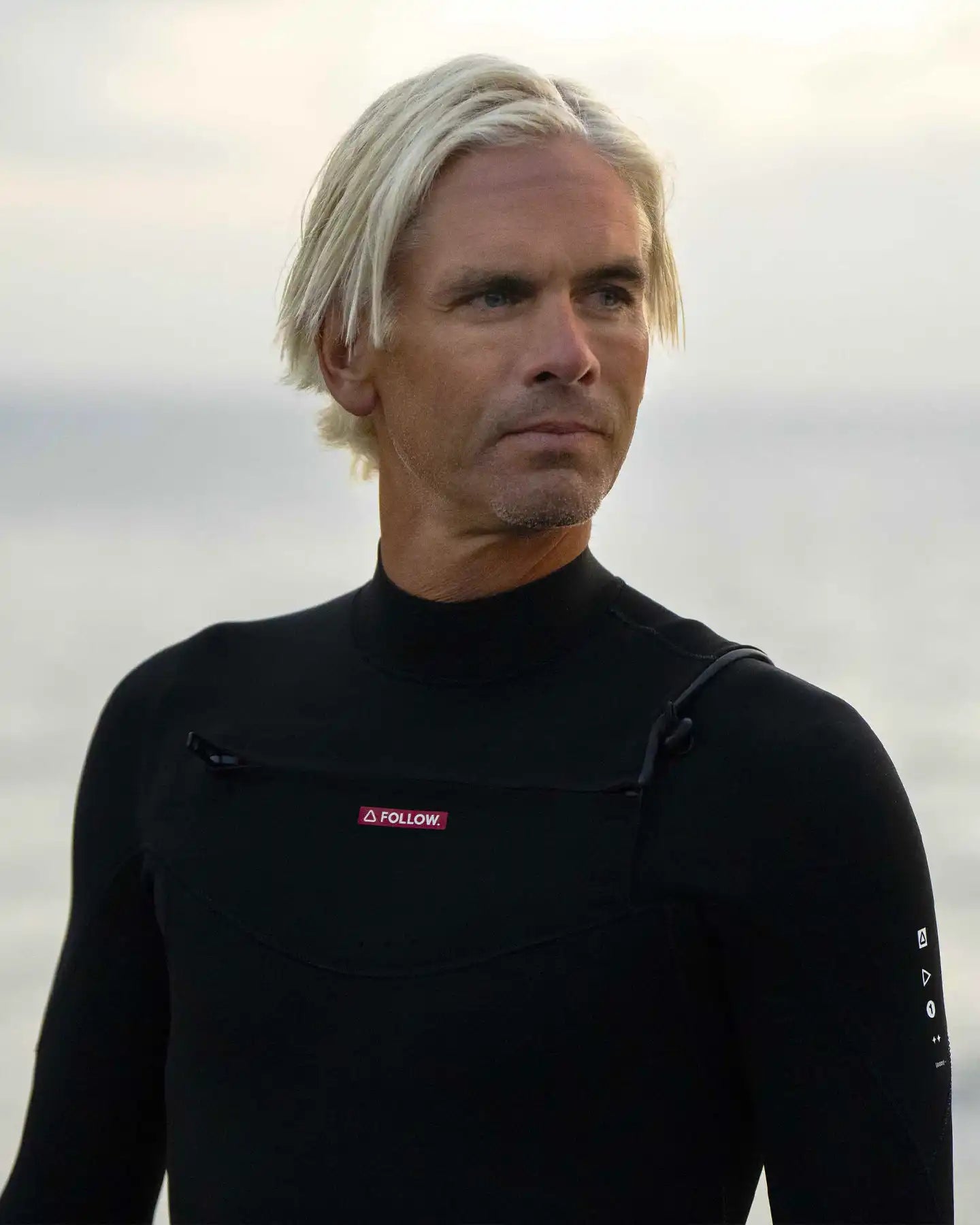 Man wearing a black wetsuit with a visible brand logo against a neutral background