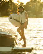 Woman holding a surfboard on a dock with sunset lighting