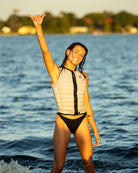 Woman in a life jacket standing in water, making a peace sign.